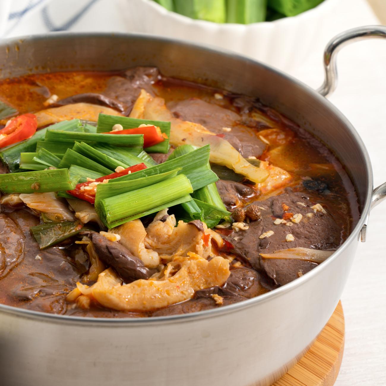Closeup image of changwang noodles made with blood curd and interstines in a pot with green onion as garnish on top